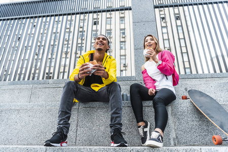 低角度观的年轻微笑多文化情侣吃汉堡包附近的滑板在城市街道