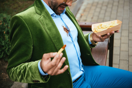 人的部分看法在绿色天鹅绒夹克与蕃茄酱在衬衣和薯条在手坐在长凳在街道上
