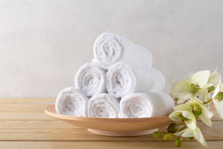 白色干净毛巾卷与花在木桌上