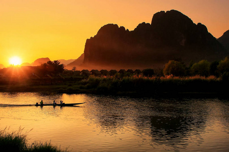 夕阳在南松河与剪影的岩层和老挝万荣一艘船。万荣是石灰岩岩溶景观冒险旅游热门目的地