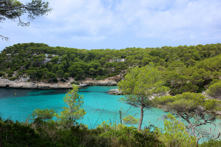 美丽的海湾在卡拉 Mitjana, 梅诺卡岛, 在西班牙的阿里岛。人们在绿松石海水中游泳和浮潜。夏季家庭假期的理想目的地