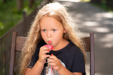 可爱的高加索小女孩坐在木椅上, 吃着甜甜的粉红色玛卡龙独自一人户外