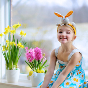 小女孩装饰的窗口与春天的花朵和复活节彩蛋。照看植物的孩子。幼儿照顾风信子和水仙花。复活节家庭内饰和装饰