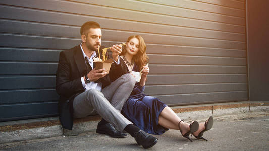 情侣在时尚服装与亚洲外卖食品坐在街上