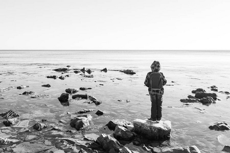 一个男孩站在黑色的大海中的岩石和水看起来
