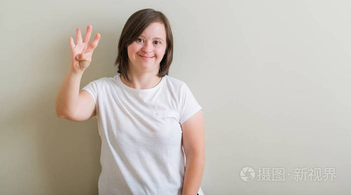 唐氏综合症妇女站在墙上显示和指向手指数四, 而微笑着自信和快乐