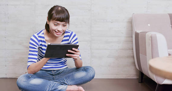 女人坐在地板上, 在家中愉快地使用平板电脑