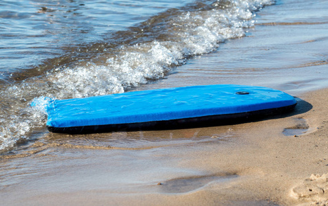 一只明亮的蓝色沙滩板在密歇根湖的海滩上冲刷海岸。