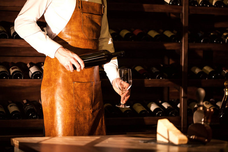 侍酒师拿着一瓶酒和玻璃在他的手中。葡萄酒的存储库位置