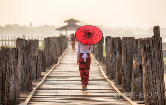 缅甸女人抱着传统的红伞和在乌本桥上行走