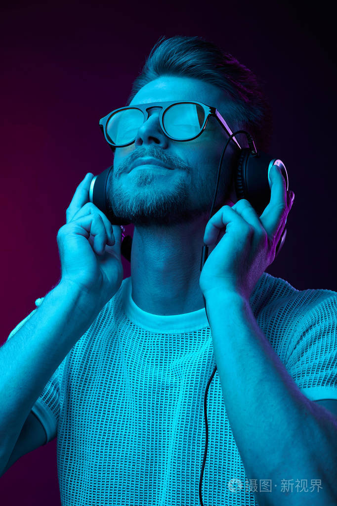 戴眼镜的帅哥喜欢用耳机听音乐.霓虹灯工作室肖像