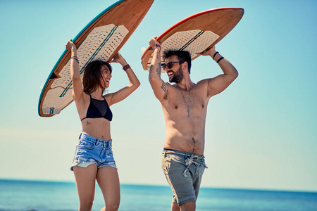 冲浪者在海滩上微笑的年轻夫妇的冲浪者在海滩上散步和在暑假里玩得开心。极限运动