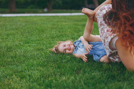 女人穿着浅色的衣服和微笑的小可爱孩子躺在绿草公园休息玩耍, 玩得开心。妈妈小女儿母亲节, 爱家庭, 亲子, 童年概念