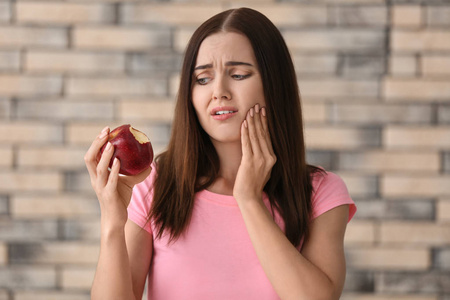 敏感的牙齿和苹果的年轻妇女在模糊的背景