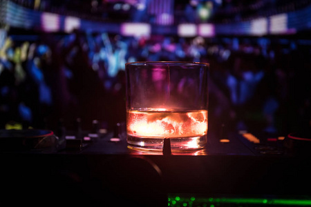 在夜总会的 dj 控制器内有带有冰块的威士忌玻璃杯。Dj 控制台与俱乐部饮料在夜总会的音乐晚会与迪斯科灯。选择性聚焦