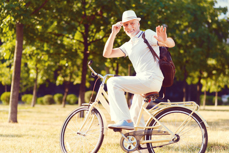 友好的退休男子坐在自行车和招呼某人在公园