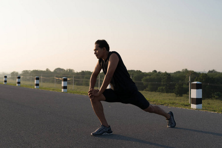 亚洲青年赛跑运动员做伸展运动, 准备在日出的时候在大坝公路运动背景下运行。健康的生活方式