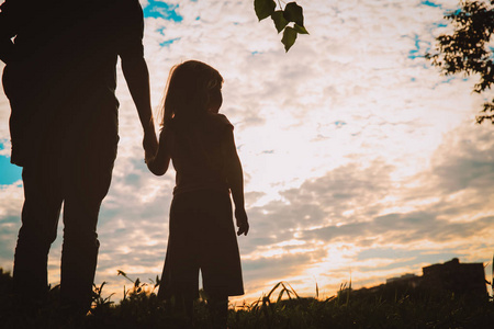 父亲和女儿手牵着手在日落时的剪影照片