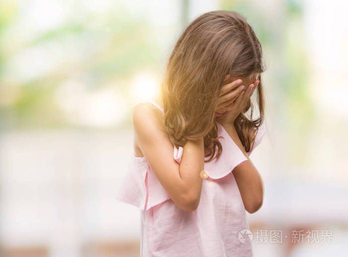 黑发西班牙裔女孩穿着粉红色的礼服与悲伤的表情覆盖脸与手, 而哭.