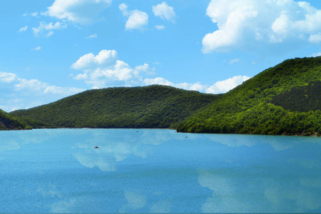 山上有森林的湖岸, 天空上有云彩的背景, 云在水中反射