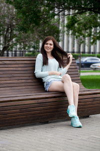 年轻漂亮的女孩坐在夏天公园的长椅上