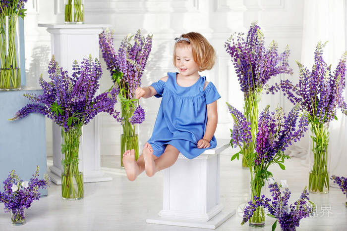 美丽的小情感女孩坐在紫罗兰色的花朵中间.室内花卉装饰