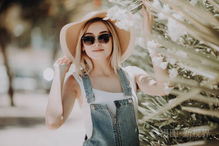 年轻的女人戴帽子, 坐在附近的玫瑰灌木在城市街道上的夏天