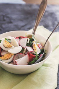 蔬菜素食沙拉的 ramson, 萝卜, 葱和煮鸡蛋与酸奶敷料在一个白色的盘子与餐具在一个深色的具体背景, 在复古加工。特写, 顶