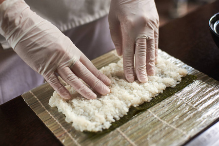 滚动寿司制作过程的特写视图。紫菜和白米在竹垫上。厨师的手摸米饭。厨师开始烹调寿司