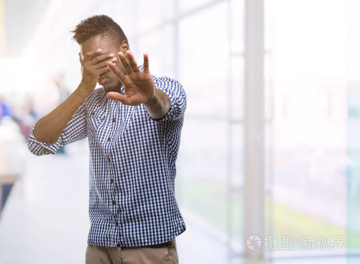 年轻的非洲裔美国人穿着蓝色衬衫, 用手捂着眼睛