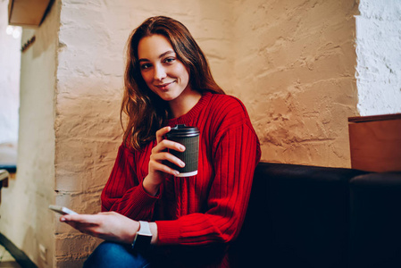 积极的十几岁女学生的肖像拿着咖啡杯看着相机, 微笑的时髦女孩休息在 coworking 空间持有智能手机连接到 wifi 博客和