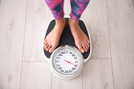 妇女测量她的体重使用秤在地板上, 以上视图照片