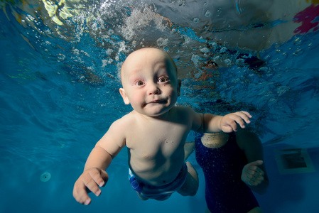 快乐宝贝婴儿水下游泳在游泳池一个蓝色的背景上。底视图。特写镜头。水平方向