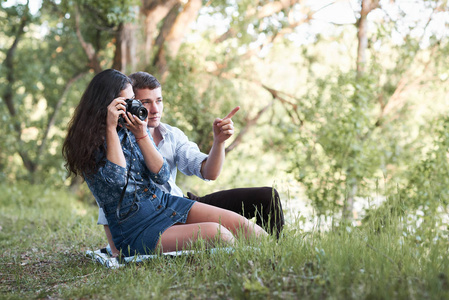 年轻夫妇坐在草地上的森林, 拍照和看日落, 夏季自然, 明亮的阳光, 阴影和绿叶, 浪漫的感觉