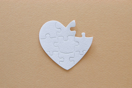 顶部视图图像的纸白色的心拼图与缺失片棕色柔和的背景。卫生保健捐赠世界心脏日和世界卫生日概念