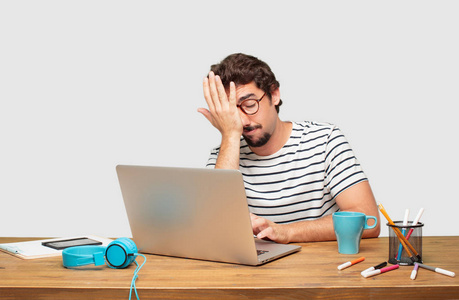 年轻的胡子图形设计师与笔记本电脑看起来冷淡和无聊, 听一些枯燥乏味