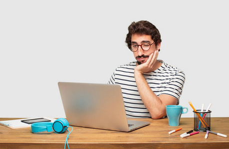 年轻的胡子图形设计师与笔记本电脑看起来冷淡和无聊, 听一些枯燥乏味