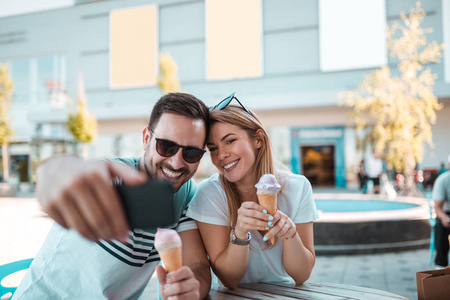 戴太阳镜的年轻人正在和女友自拍, 而他们在户外吃冰淇淋。