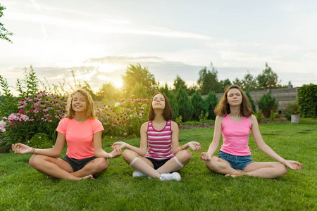 一群年轻的少女练习瑜伽, 冥想, 坐在草地上的莲花位置附近的房子