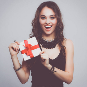 年轻女人幸福的微笑举行礼品盒在手中，在灰色的背景中分离
