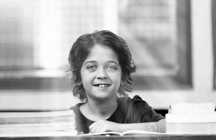 白人小学生在小学, 快乐在他的办公桌, 太阳光线来自外面