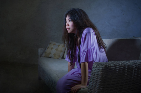 孤独无助年轻的悲伤和沮丧的亚洲华人妇女独自哭泣绝望地坐在家里沙发