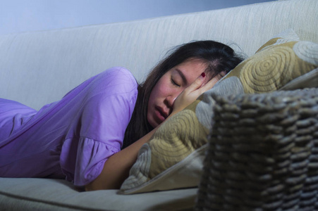 年轻的悲伤和沮丧的亚洲日本妇女独自哭泣绝望和担心在痛苦坐在家里沙发沙发遭受抑郁症和焦虑问题感到孤独无助