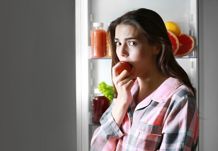 女人吃从冰箱里的番茄
