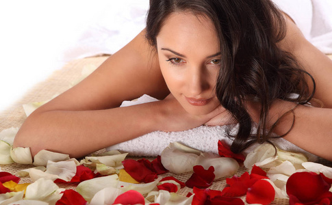在健康水疗按摩治疗躺在竹桌上的白毛巾快乐轻松的美女装饰着玫瑰花瓣
