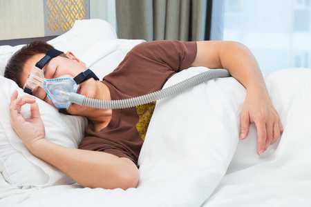 软管连接亚洲男子穿着 cpap 口罩, 连接到空气软管, 睡在他的床上, 在