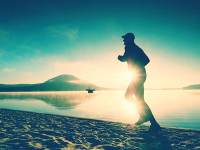 轮廓的运动积极的人在日出时在湖滩上运行.健康的生活方式照片