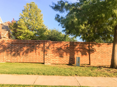 红砖细分墙在欧文, 得克萨斯州, 美国, 邻里住宅之间的屏障和公共权利的方式繁忙的街道与路径。屏幕声音转向墙和击剑系统