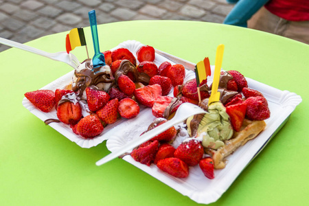 美味的冰淇淋与草莓在绿色的桌子上。比利时的小旗作为装饰品。根特市