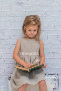 女孩, 婴儿穿着白色砖墙背景与手提箱, 与书